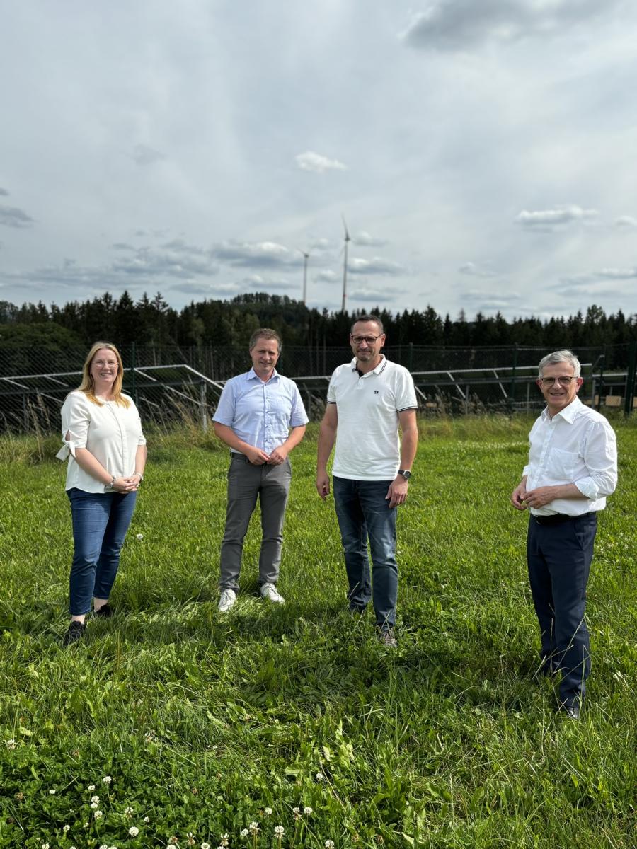 Vier Personen stehen auf einer Wiese vor einem Solarfeld