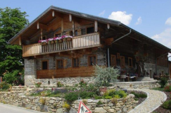 Ein niederbayerisches Waldlerhaus mit Balkon wurde renoviert und steht auf einem mit Steinen befestigten Hügel.