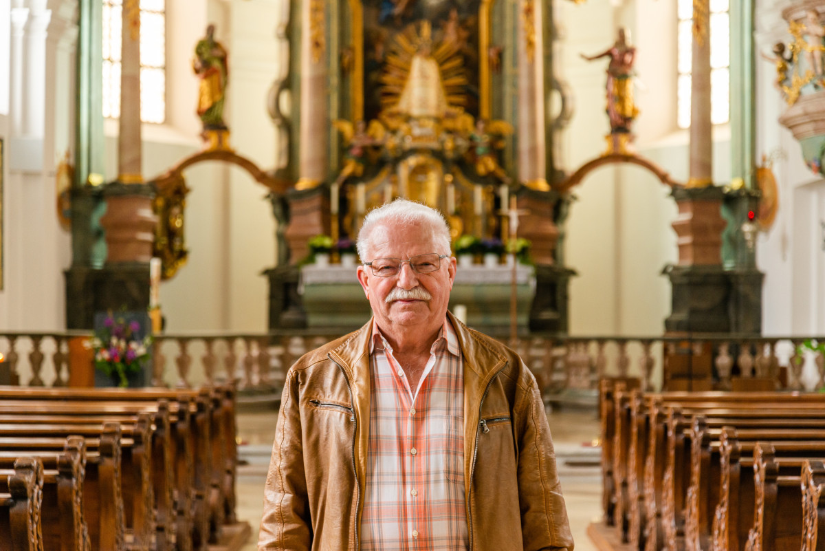 Das Bild zeigt eine Halbtotale von Georg Schmidbauer in der Kirche von Waldthurn. Links und rechts im Bild sind die Kirchenbänke zu sehen. Im Hintergrund sieht man den verzierten Altarraum.