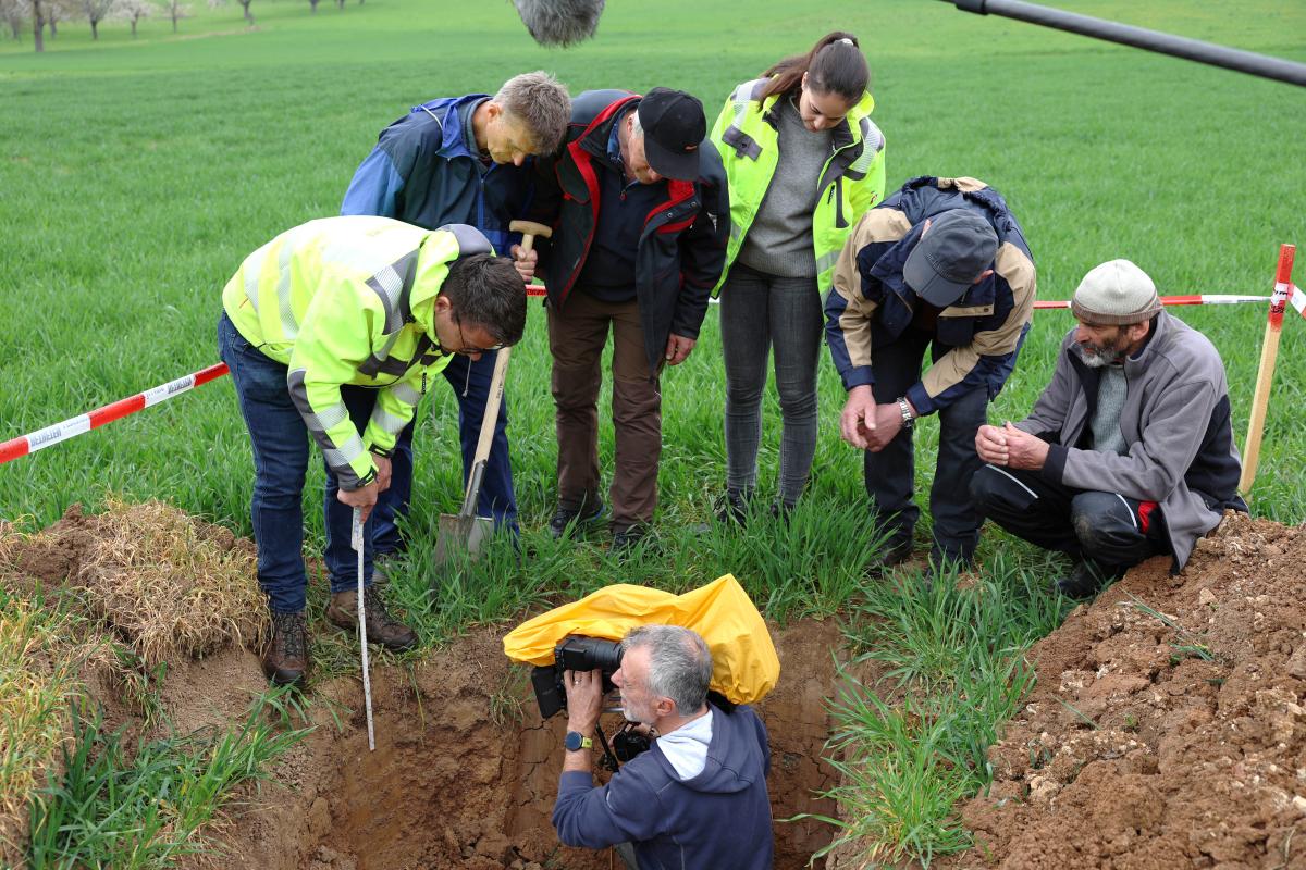 Ein Mann mit Kamera filmt aus einer Erdkuhle heraus, sechs Personen stehen am Rand