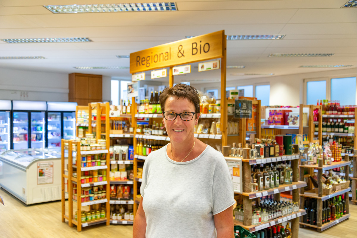 Halbtotale von Petra Reil im Marktladen. Im Hintergrund sind die Regale mit den Waren zu sehen.