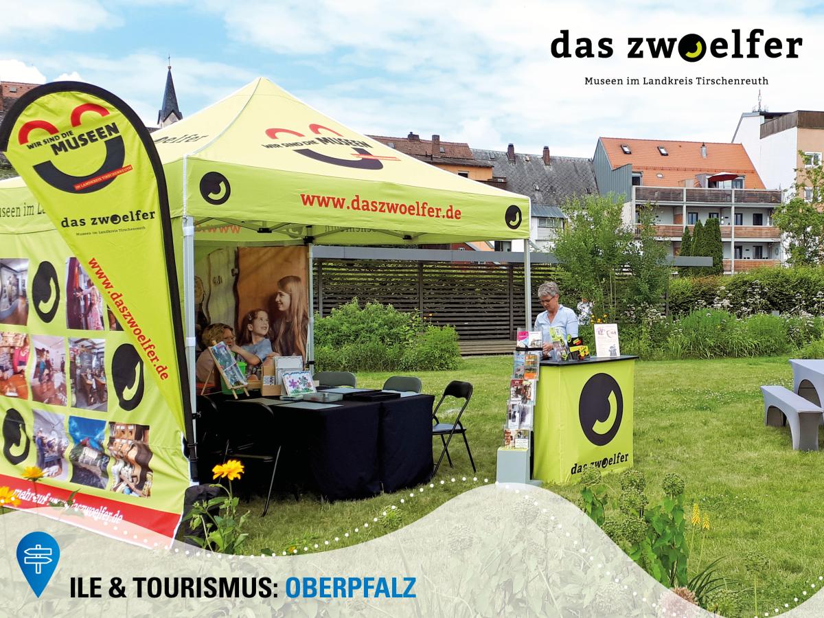 Ein Pavillon und eine Beachflag mit dem Design "das zwoelfer" steht auf einer Wiese