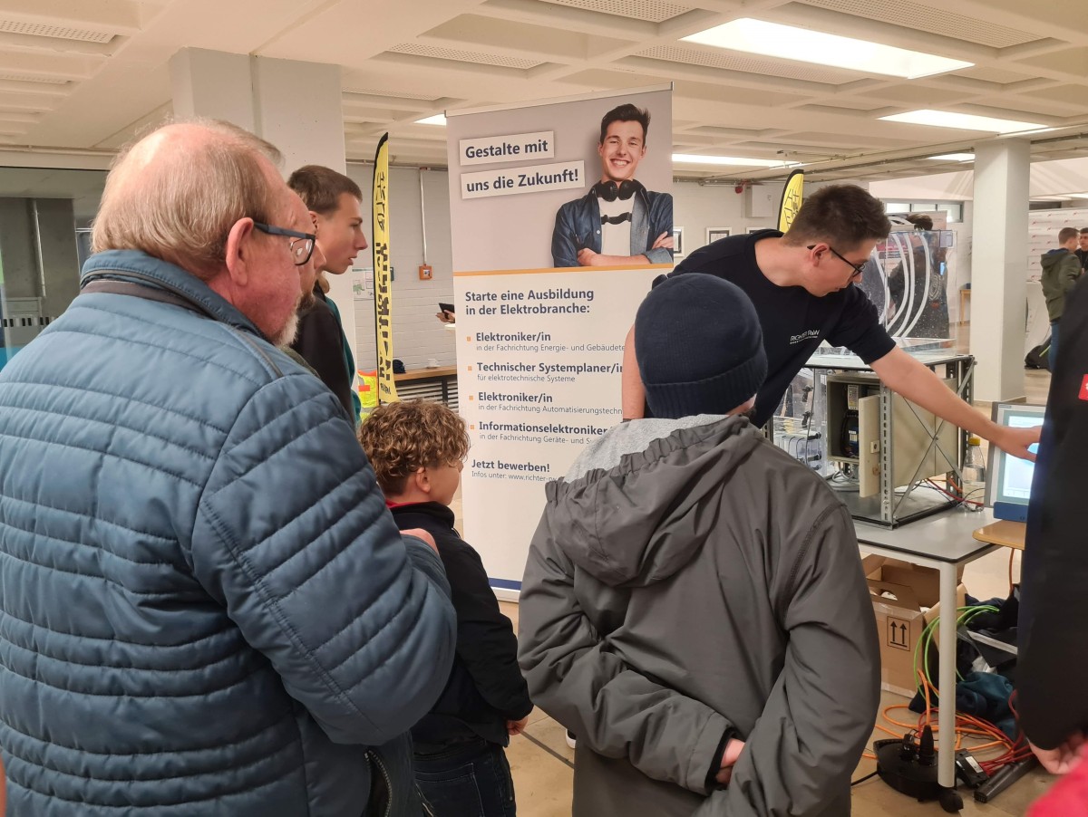 Besucher der Messe hören gespannt den Ausführungen eines Mitarbeiters zu.