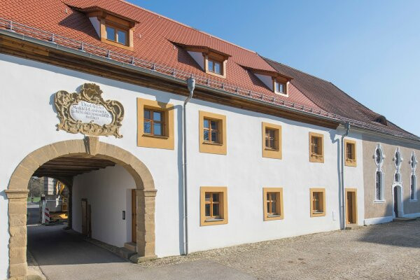 Die Fassade eines zweistöckigen Klosters erhält ockergelbe Fensterumrahmungen und eine weiße Fassade