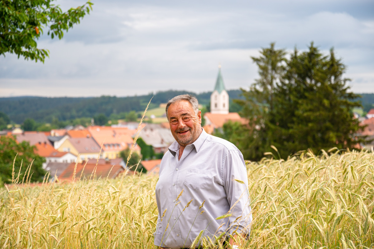 Halbtotale des Bürgermeisters von Waldthurn, Josef Beimler draußen in einem sommerlichen Kornfeld. Im Hintergrund sieht man die Häuser von Waldthurn