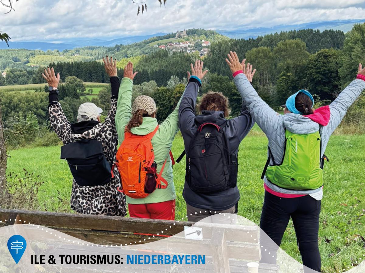 Vier Wanderer heben die Hände in die Höhe und blicken dabei auf eine fantastische Hügellandschaft.