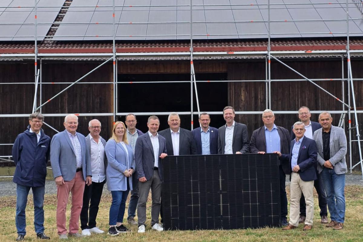 Alle Beteiligten des Pressetermins stehen vor einem Gebäude mit Dach_PV-Anlage