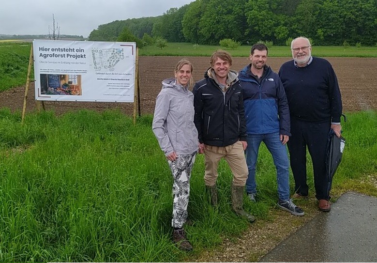 Vier Personen stehen an einer Landstraße vor einem Schild