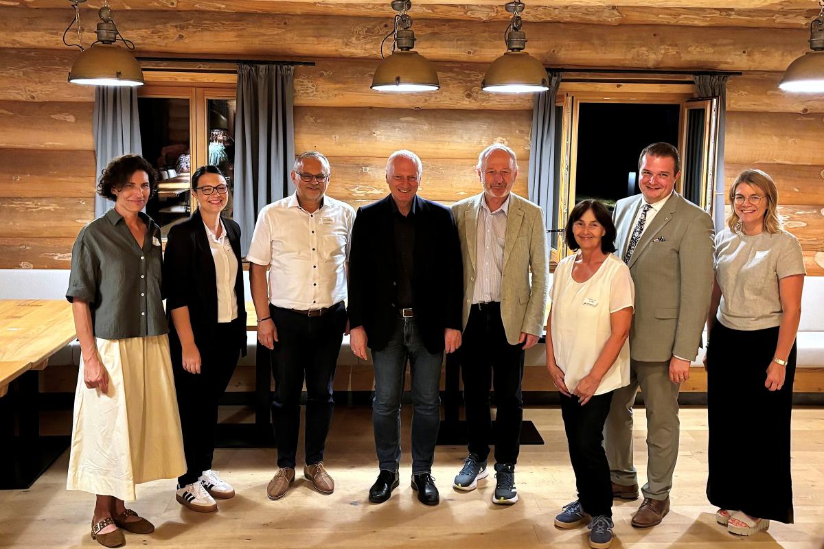 Team der Schwammregion: Acht Personen stehen nebeneinander in einem rustikalen Raum mit Holzwänden und hängenden Lampen
