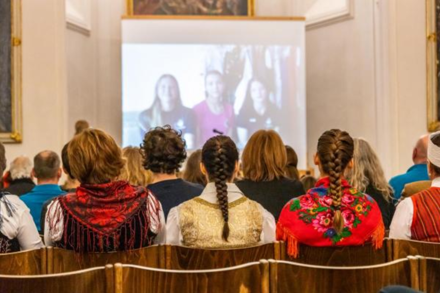 Jugendliche in Tracht lauschen einem Vortrag