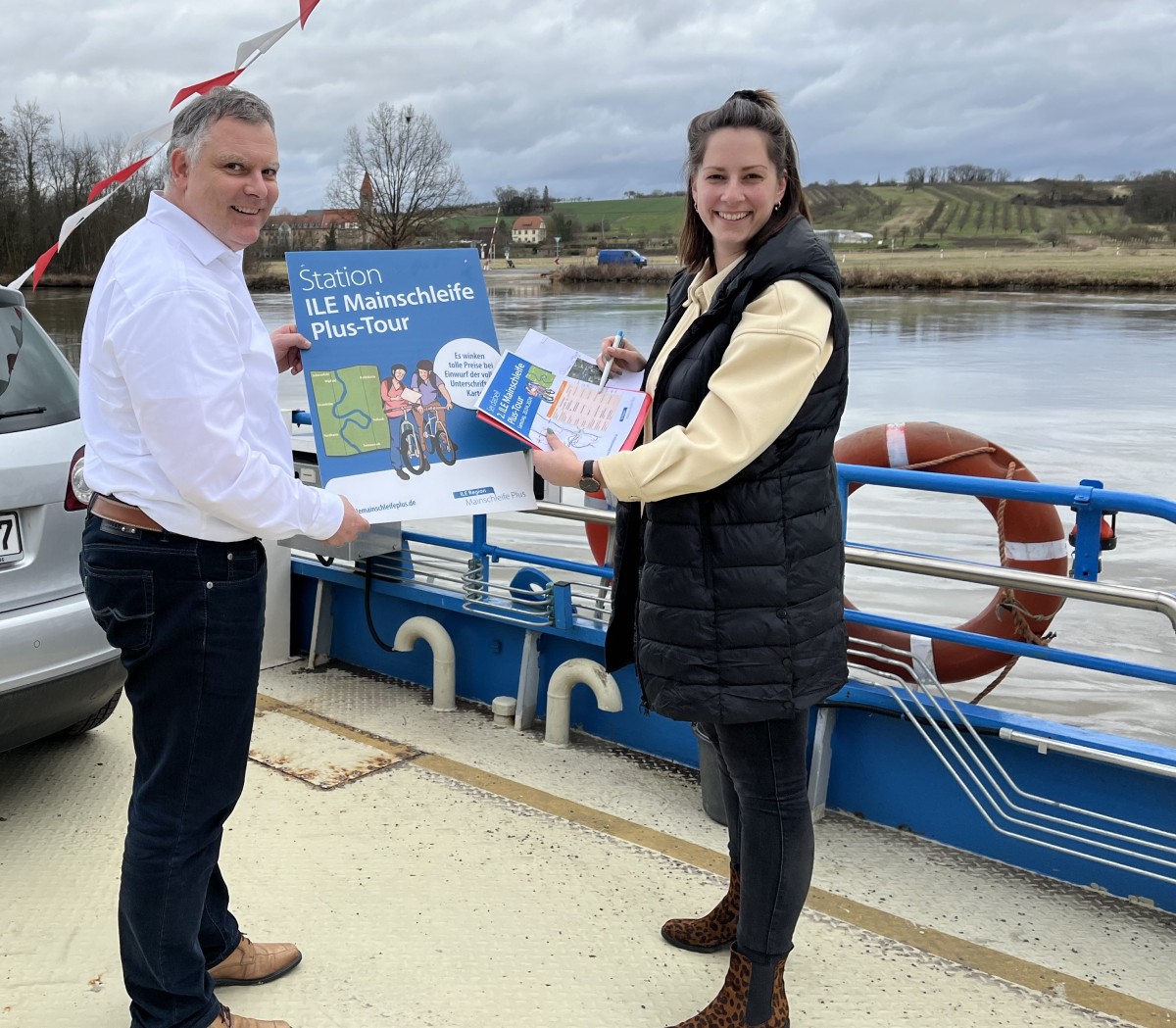 Ein Mann und eine Frau stehen am Flussufer und haben Flyer in der Hand.