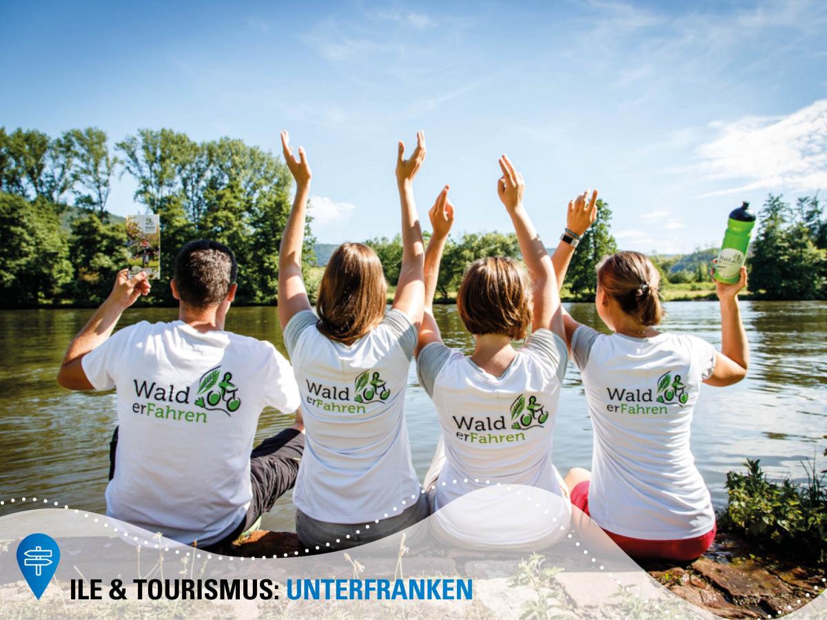Vier Personen mit einem weißen Shirt und Aufdruck WalderFahren sitzen auf einem Steg an einem See und jubeln.